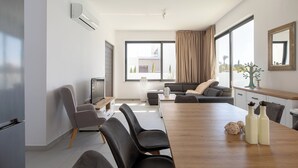 Een moderne woonkamer met een houten eettafel, zwarte stoelen, een grijze bank en een groot raam met gordijnen.