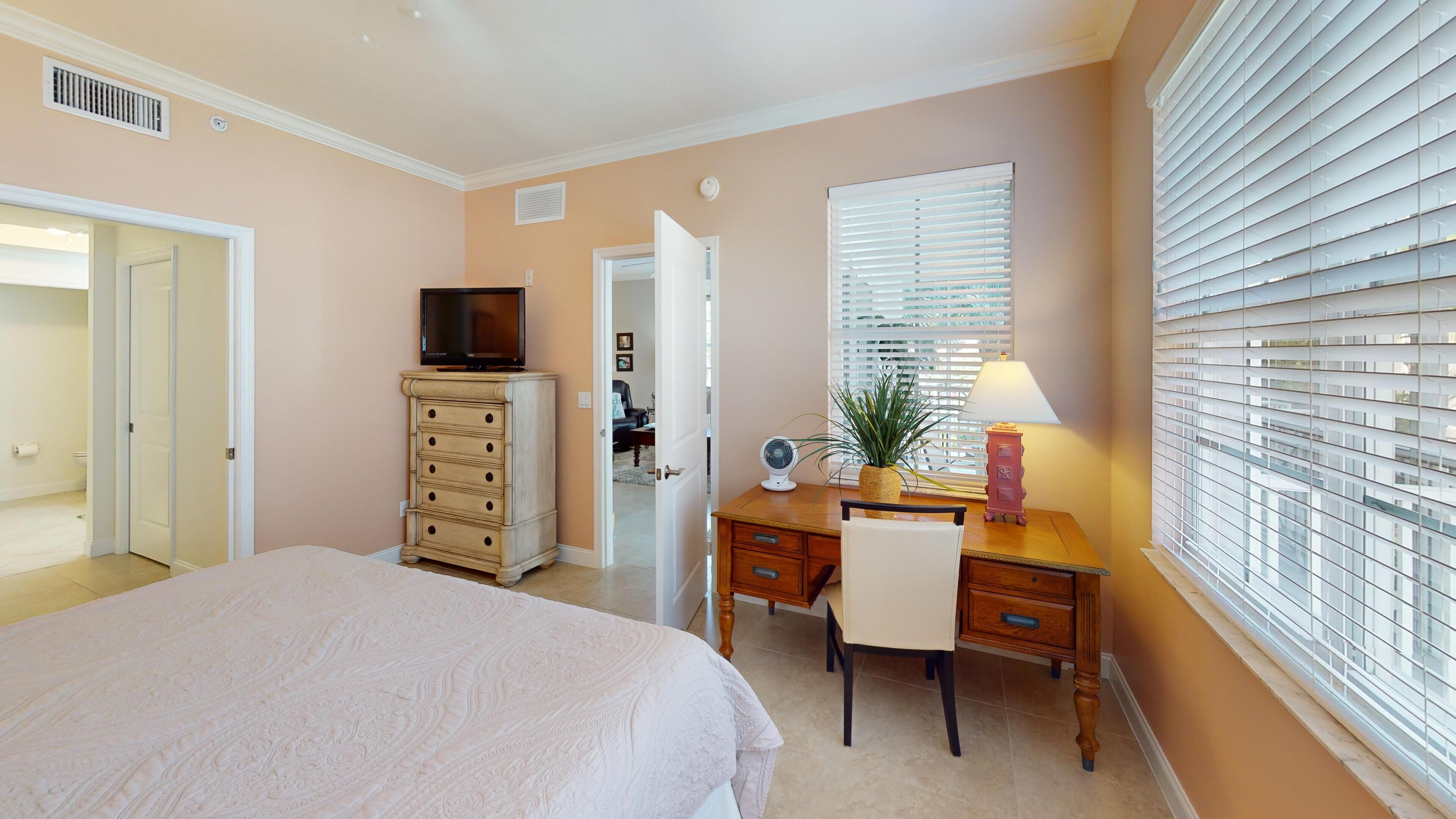 A bedroom with a bed, dresser, desk, and window with blinds.