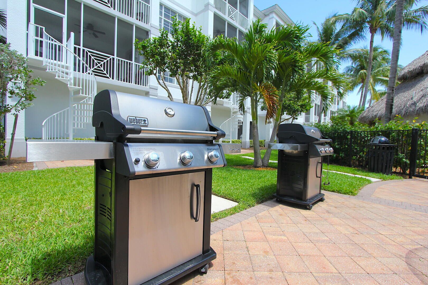 A barbecue grill with a digital display and multiple control knobs, situated on a paved patio with a well-maintained lawn and palm trees.