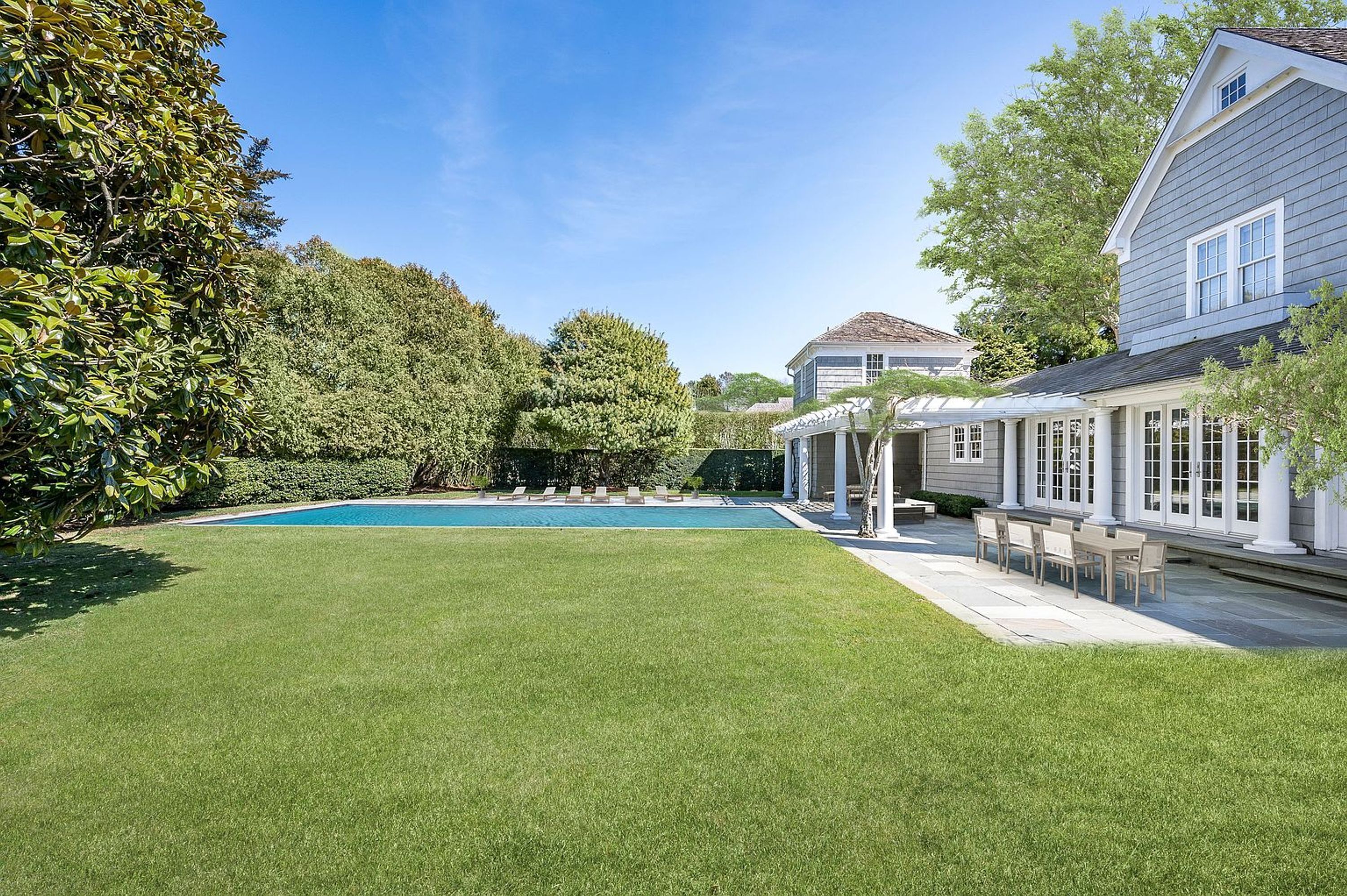 A backyard with a swimming pool, a patio with outdoor furniture, and a house with a covered porch.