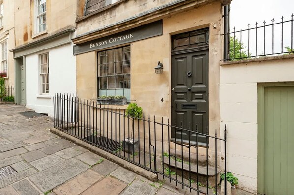 A building labeled "BENSON COTTAGE" with a black metal fence, a green door, and a window with blinds. - Luxury Cottage in the Heart of Bath (Bath)