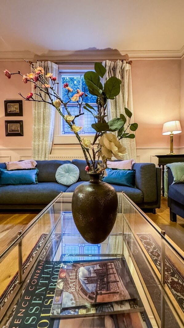 A living room with a glass coffee table, a vase with flowers, a sofa with cushions, and a lamp. - Luxury Cottage in the Heart of Bath (Bath)