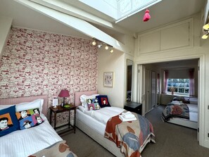 A bedroom with two beds, a patterned wallpaper, a small table with a lamp, and a window with curtains. - Luxury Cottage in the Heart of Bath (Bath)