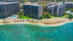 Luftaufnahme einer Küstenhotelanlage mit mehreren Hochhäusern, einem Sandstrand und klarem türkisblauem Wasser.
