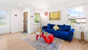 Uma sala de estar moderna com um sofá azul, uma mesa de centro vermelha e uma mesinha de apoio de vidro.