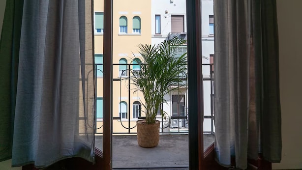 Een balkon met een bloempot, uitzicht op gebouwen en een metalen hekwerk.