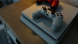 Een laptop met een gamecontroller erop, een rode gamecontroller ernaast en een lamp op de achtergrond.