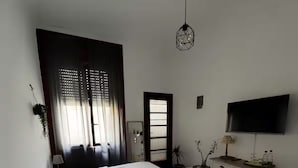 Een slaapkamer met twee bedden, een televisie, een bureau en een raam met gordijnen.