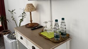 Een wit bureau met een televisie die aan de muur erboven bevestigd is. Op het bureau staan twee planten in potten, een lamp en een dienblad met waterflessen en glazen.