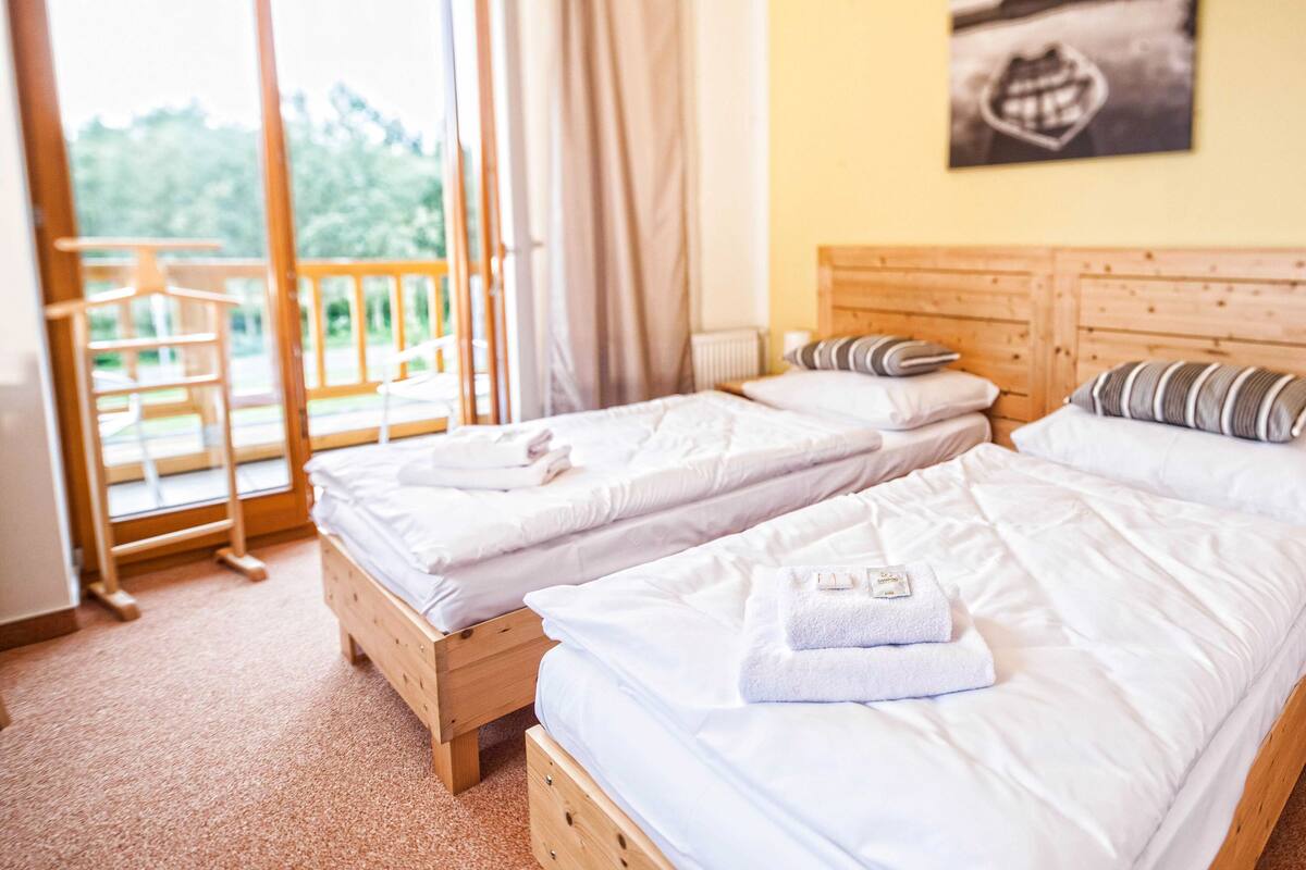 Une chambre d’hôtel avec deux lits, des têtes de lit en bois et un balcon donnant sur un paysage verdoyant.