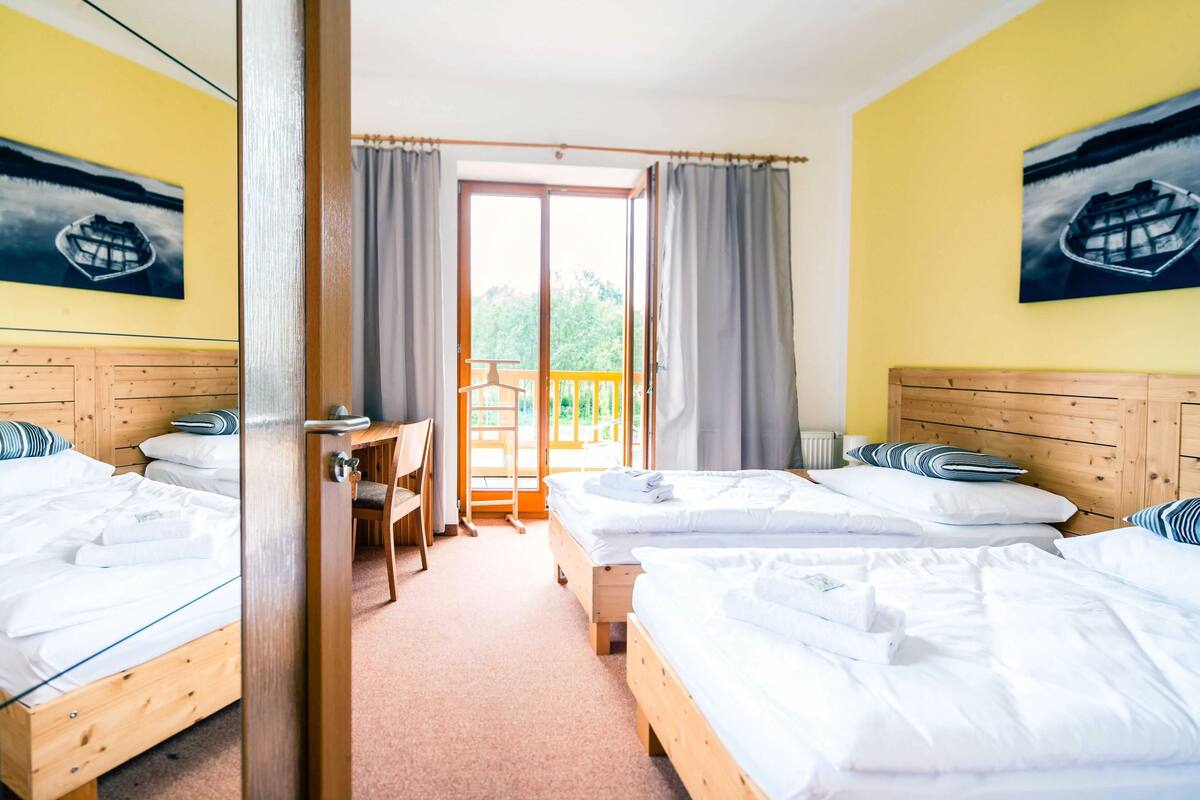 Une chambre d’hôtel avec deux lits, une tête de lit en bois, un bureau et un balcon avec des rideaux.