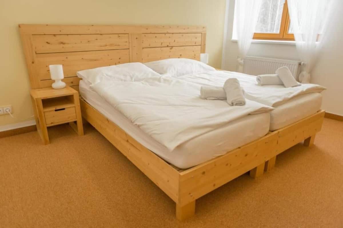Un lit en bois avec du linge de lit blanc et une table de chevet avec une lampe blanche.
