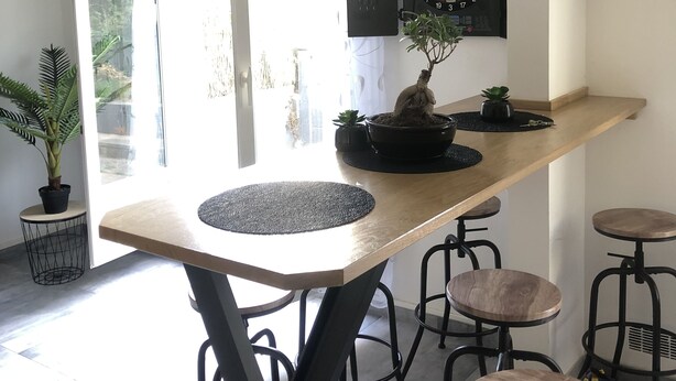 A modern kitchen with a wooden bar counter, bar stools, a dartboard, and a clock on the wall. - House rental for 24h of Le Mans, Le Mans Classic and Grand Prix events (Parigné-l'Évêque)