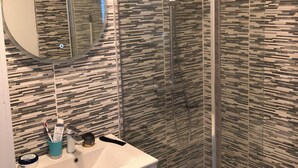 A modern bathroom with a glass-enclosed shower, a white sink with a mirror, and a patterned wall. - House rental for 24h of Le Mans, Le Mans Classic and Grand Prix events (Parigné-l'Évêque)