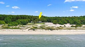 Un paysage côtier comprenant une plage, une colline boisée et un bâtiment sur lequel est peinte une flèche jaune pointant vers celui-ci.