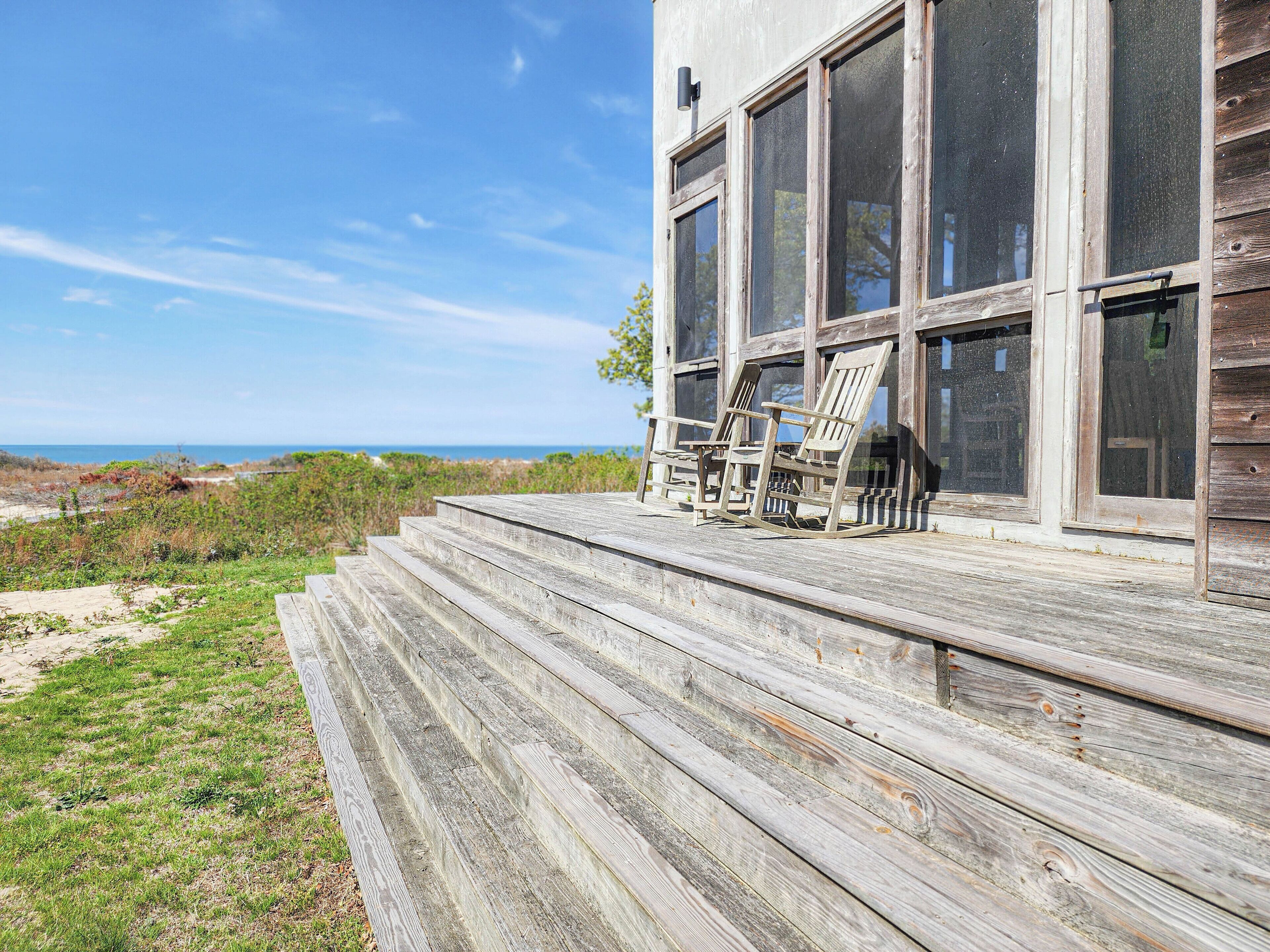 A wooden deck with steps leading to a building with large windows overlooking the beach.