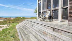 Une terrasse en bois avec des marches menant à un bâtiment doté de grandes fenêtres donnant sur la plage.