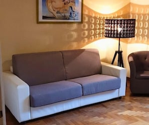 Un salon avec un canapé, un fauteuil, une lampe et un tableau au mur.