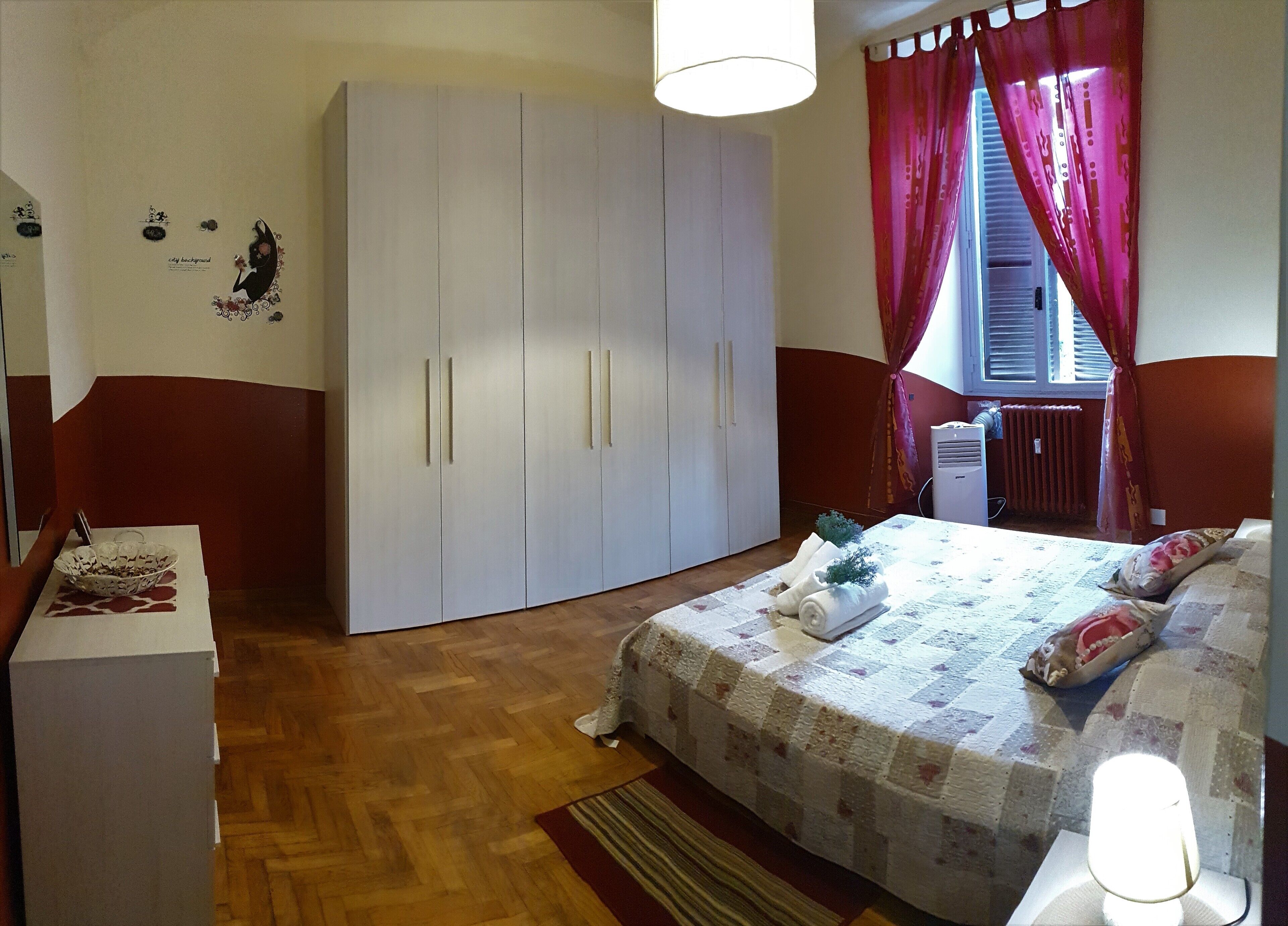 A bedroom with a large wardrobe, a bed with a floral bedspread, and a small table with a bowl.