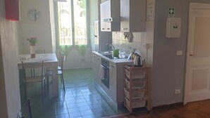 A compact kitchen with a sink, stove, and cabinets. There is a small dining area with chairs and a table. A window provides natural light, and a door leads to another room. - Casa Tua a Porta Maggiore (Rome)