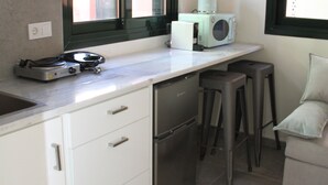 A compact kitchen with a built-in dishwasher, a microwave, and a small countertop with a coffee maker. There are two stools and a chair near the window. - Pirgos Warm Studio for 3 by MPS (Pirgos)