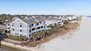 A beachfront residential area with multi-story houses, a sandy beach, and a clear sky.