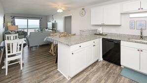 A modern kitchen with white cabinetry, a granite countertop, and a black dishwasher.