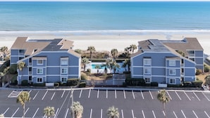 A beachfront hotel with a swimming pool and parking lot.