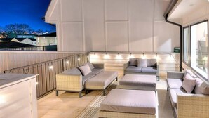 A spacious outdoor seating area with wicker furniture and cushions, a wooden floor, and a view of the cityscape at dusk. - Bright and Spacious 4 Bedroom Nash Home w/Rooftop! (Nashville)