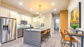 A modern kitchen with stainless steel appliances, a central island, and a dining area with wooden chairs. - Bright and Spacious 4 Bedroom Nash Home w/Rooftop! (Nashville)