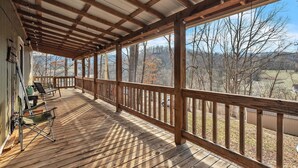 A covered deck with wooden railings, a folding chair, and a table. - Hillside Hideaway 2 Bedroom Cabin (Elizabethton)