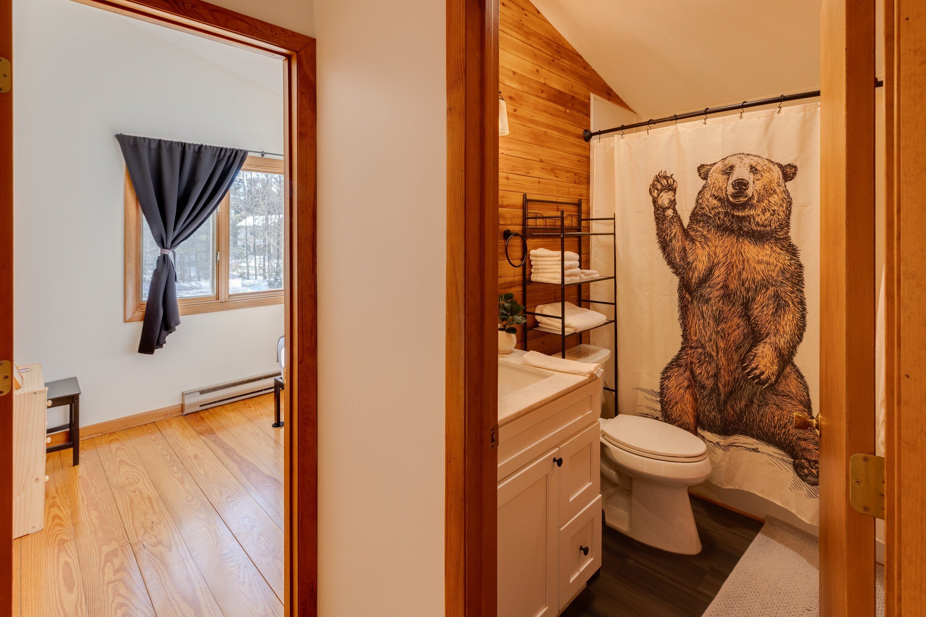 A bathroom with a wooden floor, a white sink, a toilet, and a shower curtain with a bear design.