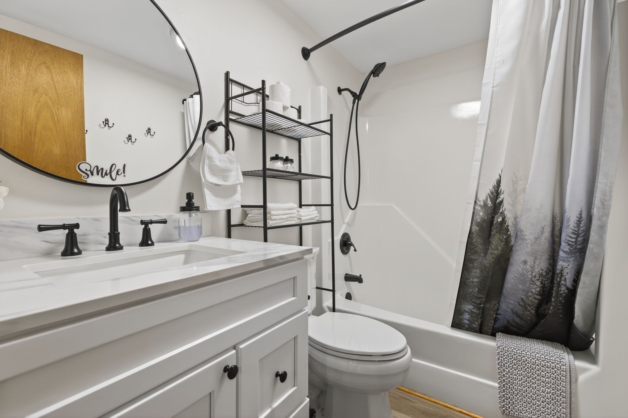 A modern bathroom with a white sink, black faucets, a toilet, a shower with a black hose, and a towel rack.