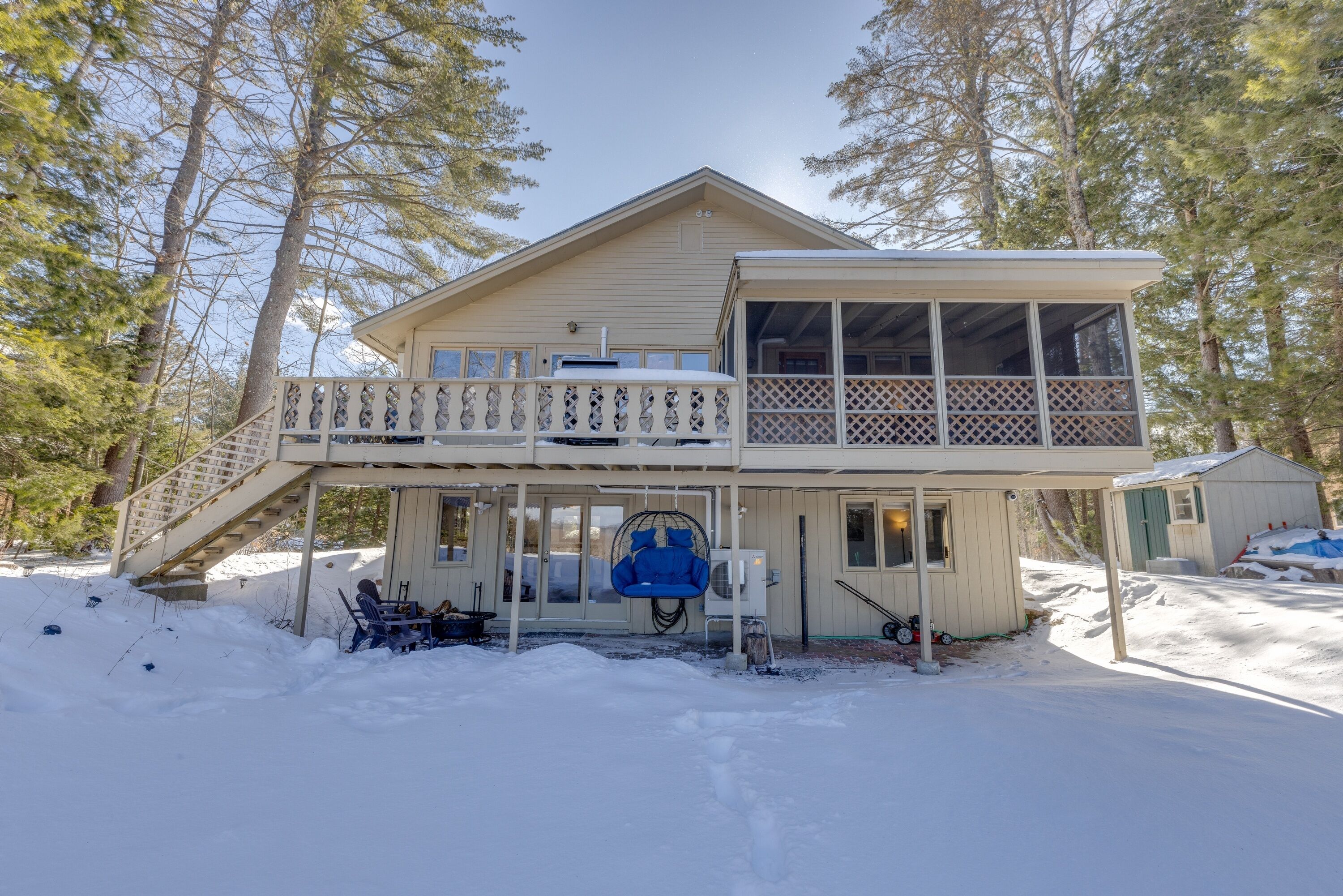 A two-story cabin with a balcony, surrounded by snow and trees.