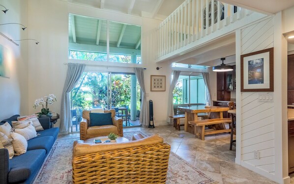 A spacious living area with a high ceiling, a balcony, and a dining area with wooden furniture.