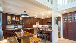 A spacious kitchen with dark wooden cabinets, a central island with bar stools, a built-in microwave, and a large window providing natural light. - Puamana at Princeville Island Style Townhome, Beautifully Updated, sleeps 8 (Princeville)