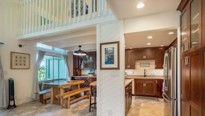 A spacious kitchen with wooden cabinets, a stainless steel refrigerator, and a dining area with a wooden table and bench. - Puamana at Princeville Island Style Townhome, Beautifully Updated, sleeps 8 (Princeville)