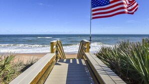 Une promenade en bois menant à la plage, avec un drapeau américain flottant sur un mât.