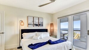 Une chambre à coucher avec un lit, une table de chevet, une lampe et une vue sur l’océan, visible à travers une porte coulissante.