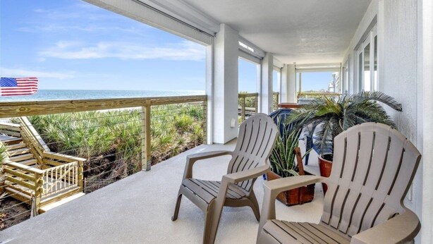 Un balcon avec deux fauteuils Adirondack, une vue sur l’océan et un drapeau américain.