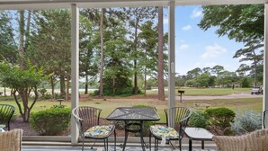 A covered patio with a table and chairs, surrounded by trees and a view of a golf course. - 11d True Blue Golf Haven Ii 2 Bedroom Home (Pawleys Island)