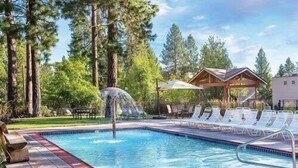 A swimming pool with a water feature, surrounded by lounge chairs and a wooden deck. - Seventh Mt 1417/1418 1 Bedroom Condo (Bend)