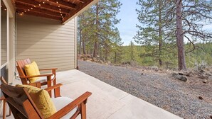 A covered porch with wooden chairs and a bench, overlooking a gravel path and trees. - Seventh Mt 1417/1418 1 Bedroom Condo (Bend)