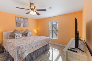 A bedroom with a bed, a ceiling fan, a window, and a TV stand.