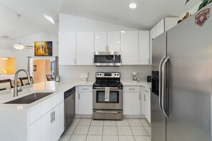 A modern kitchen with white cabinetry, stainless steel appliances, and a tiled floor.