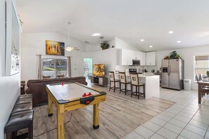A modern kitchen with a dining area, a pool table, and a living room with a sofa and a TV.