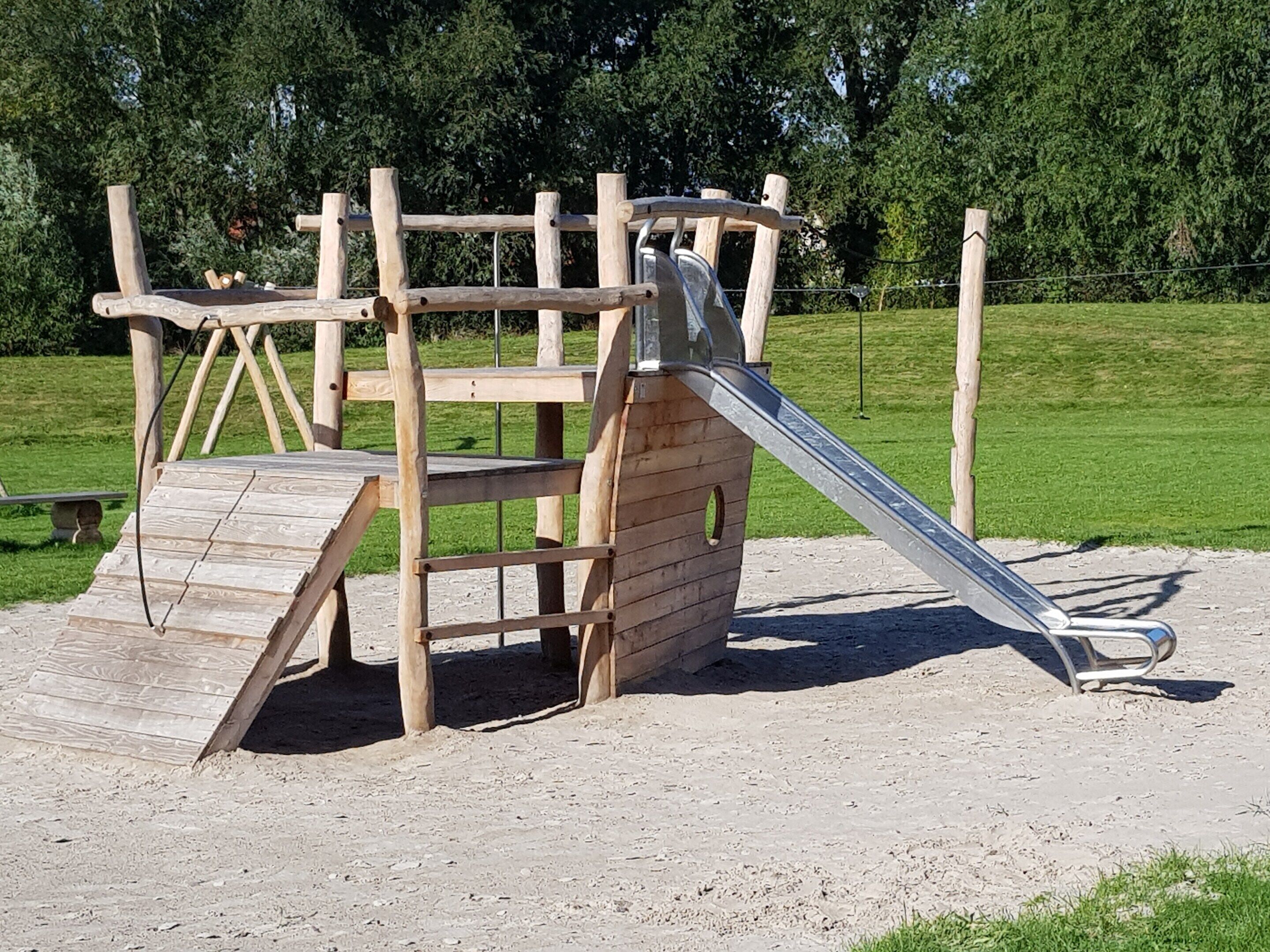 A wooden playground structure with a slide and climbing elements.