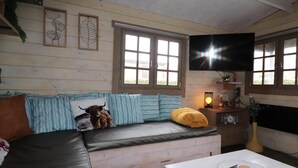L’intérieur d’un chalet confortable, avec un canapé, un téléviseur fixé au mur et une fenêtre équipée de stores.