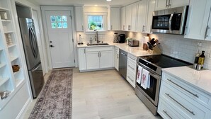 A modern kitchen with white cabinets, stainless steel appliances, and a large window. - Charming Waterfront Island Bungalow with DOCK in Narragansett! (Narragansett)
