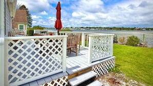 A deck with white lattice railings, outdoor furniture, and a red umbrella. - Charming Waterfront Island Bungalow with DOCK in Narragansett! (Narragansett)